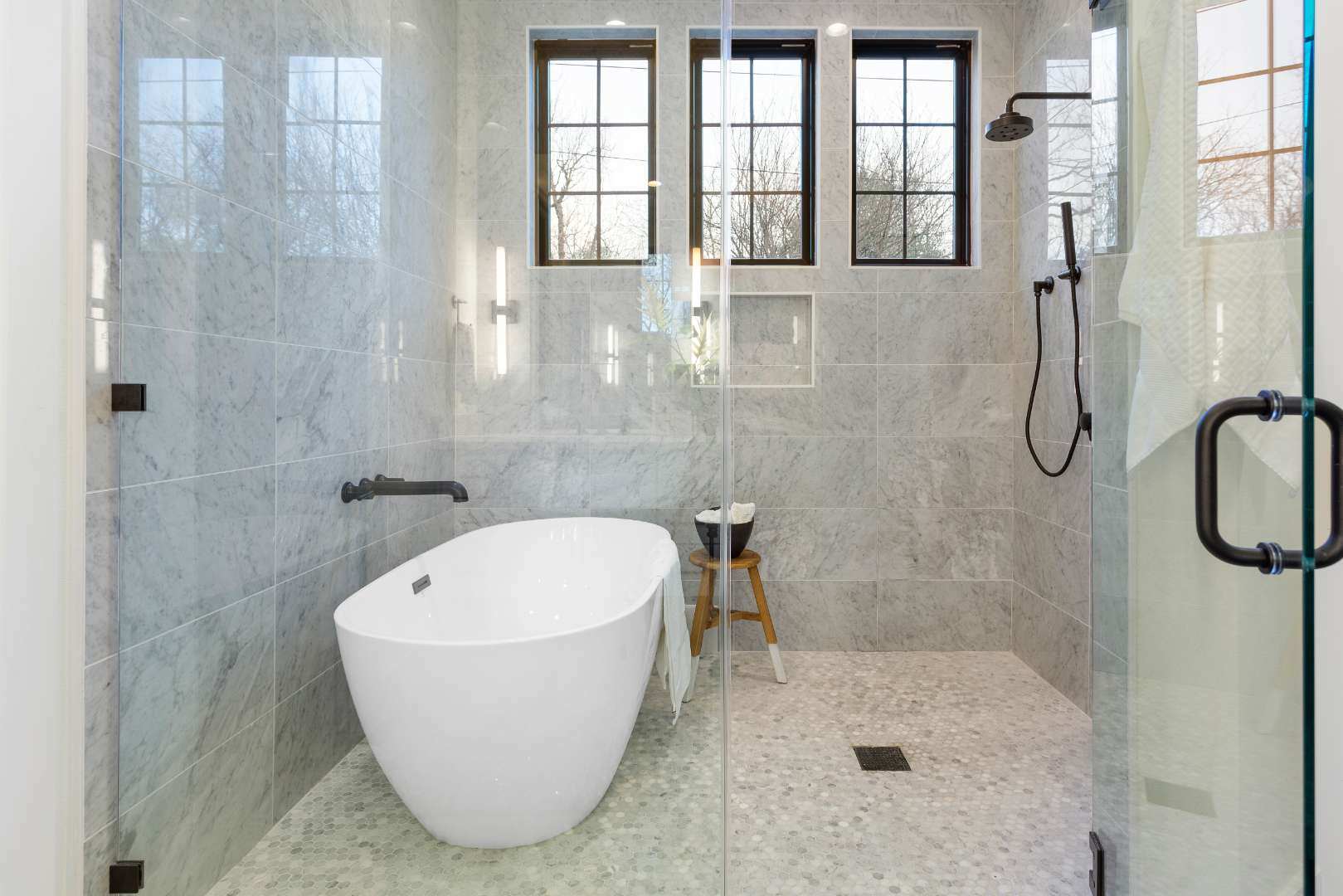 Luxurious bathroom with marble finishes: Highlights a freestanding soaking tub and a walk-in shower enclosed in glass, surrounded by marble tiles for a sophisticated look. | CKN Homes