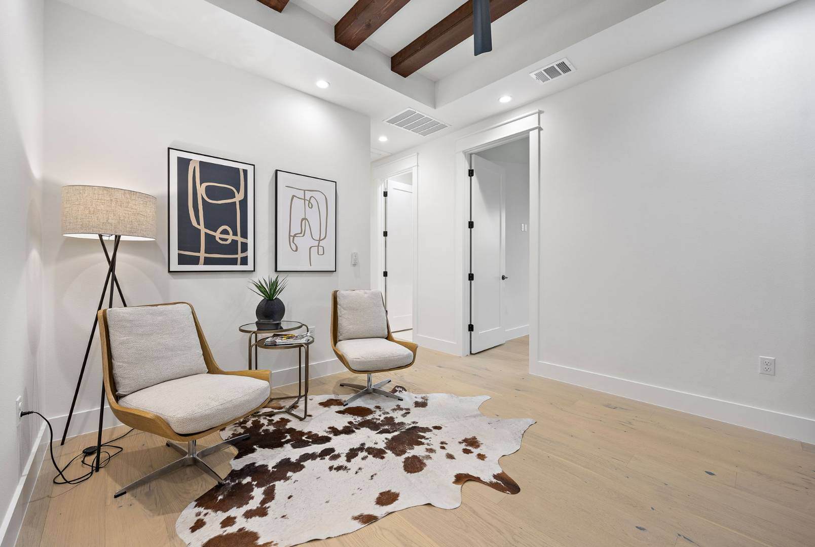 Cozy seating nook with modern decor: Showcases two upholstered chairs, a small round table, and a cowhide rug, accented by abstract artwork and exposed wood beams. | CKN Homes