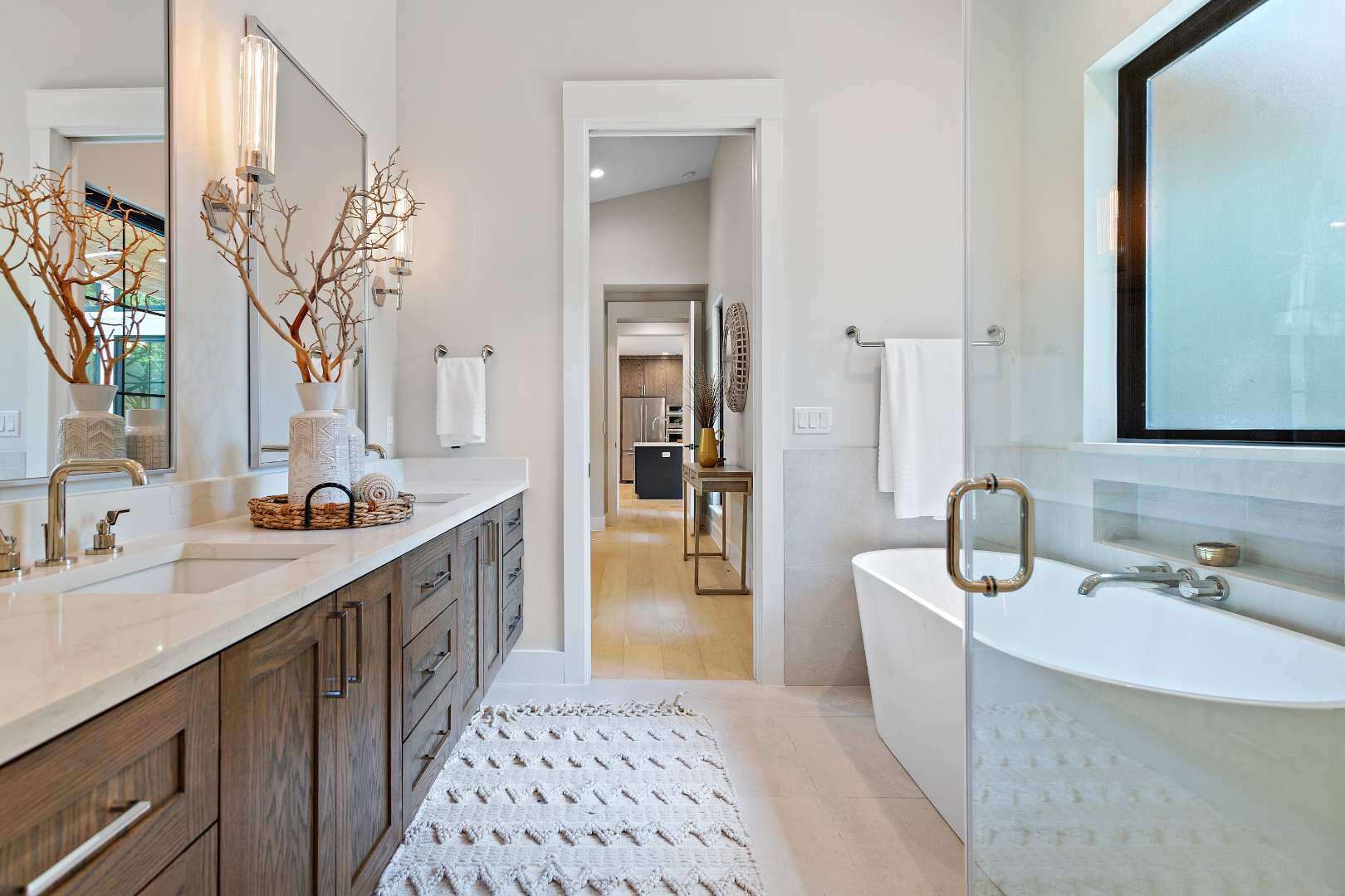 Luxurious master bathroom: Includes a freestanding soaking tub, double sink vanity with natural wood cabinetry, and decorative accents such as a woven basket and ceramic vases. | CKN Homes