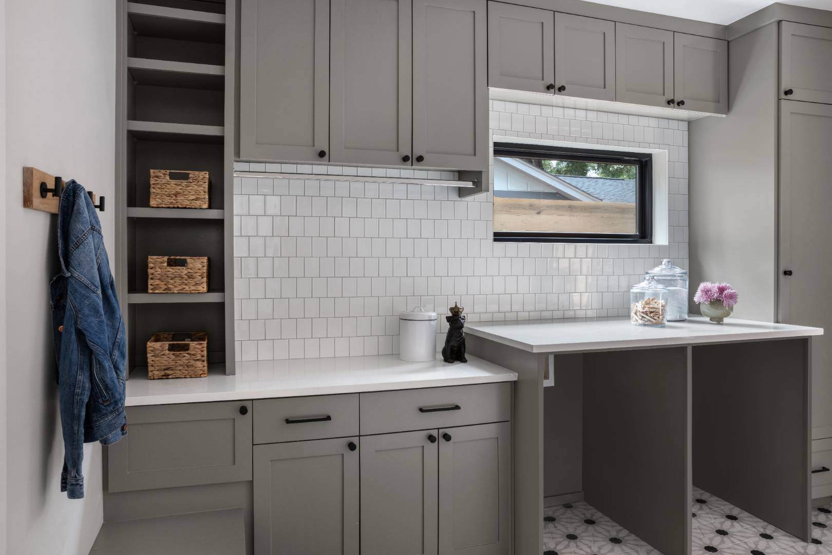 Functional laundry room: Boasts gray cabinetry, a tiled backsplash, and open shelving for storage, with a denim jacket hanging on a wall hook for added character. | CKN Homes