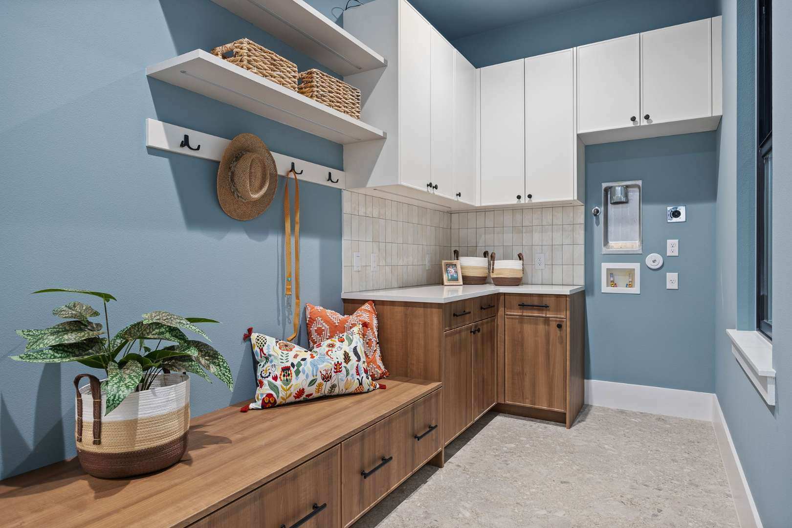 Charming mudroom with storage: Includes a built-in bench with wooden drawers, colorful pillows, and hooks for hanging hats or bags against a blue-painted wall. | CKN Homes